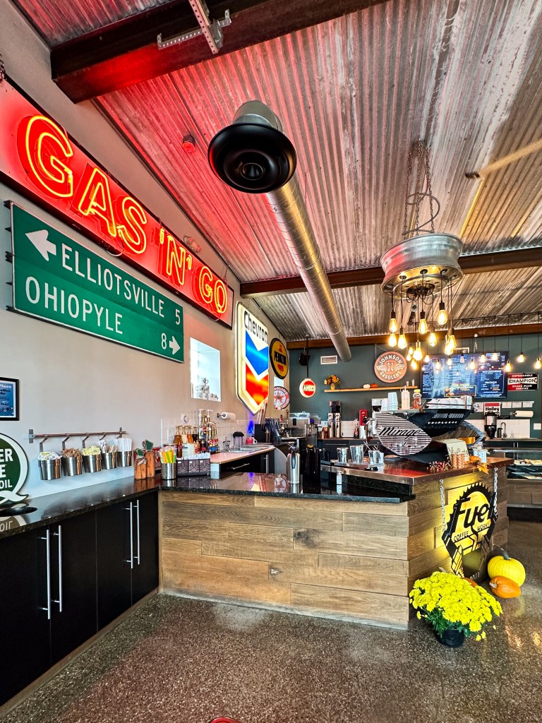Interior of Fuel Coffee Works in Farmington, Pennsylvania, featuring a vintage gas station theme with neon signs, road signs, metal decor, and a wooden counter, creating a retro, automotive-inspired atmosphere.